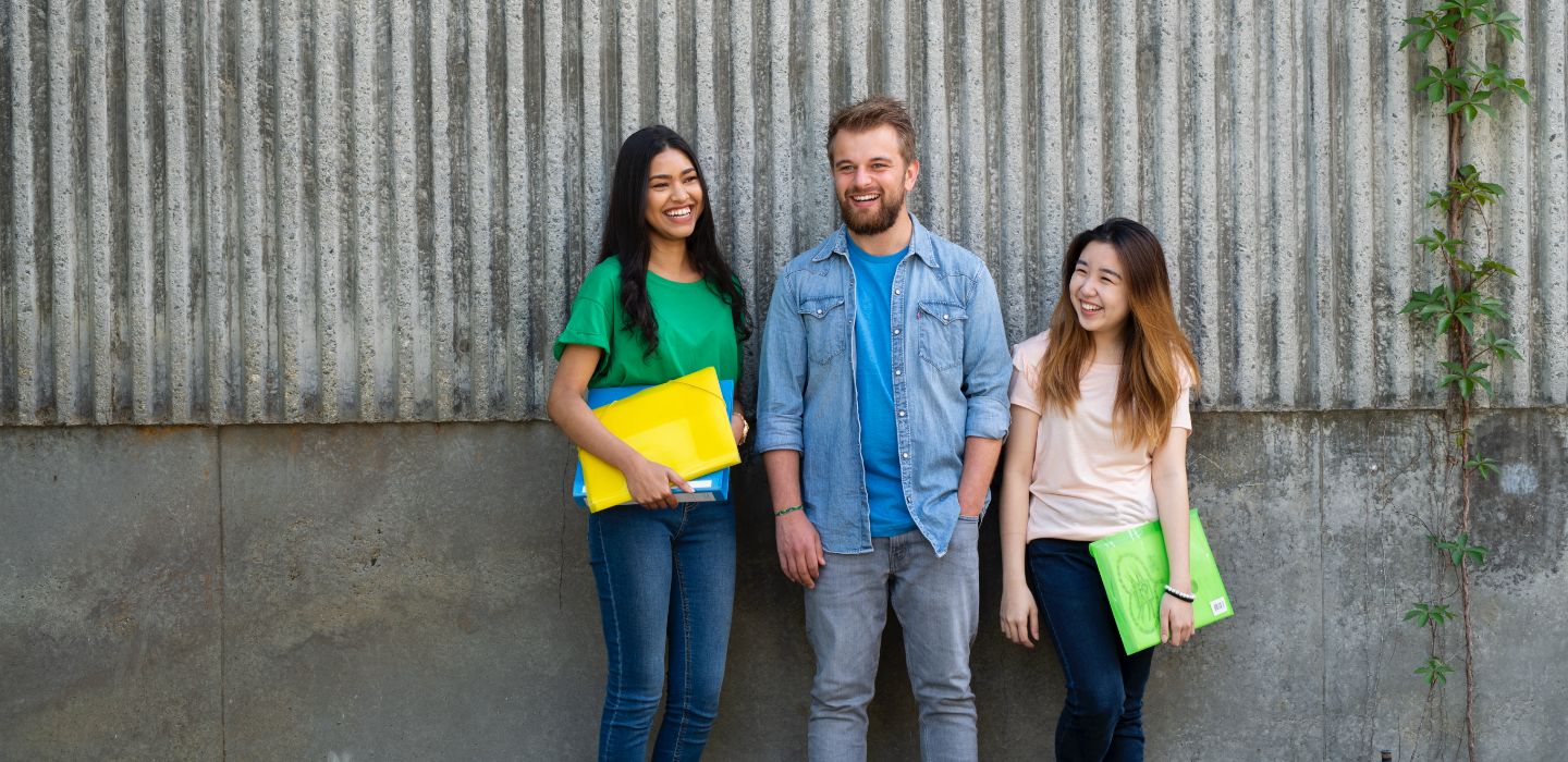 Campus group holding folders leaning on wall
