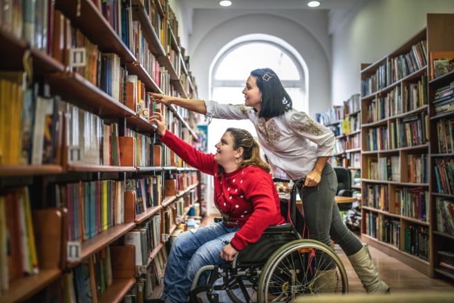Off campus female on wheelchair reaching for books